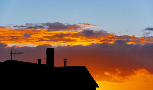 silhouette of residential building with roofs and TV antenna receiver at sunset