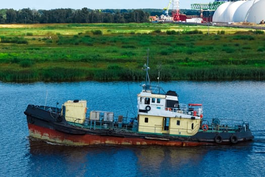 Old tug ship moving to the cargo terminal. Industrial service