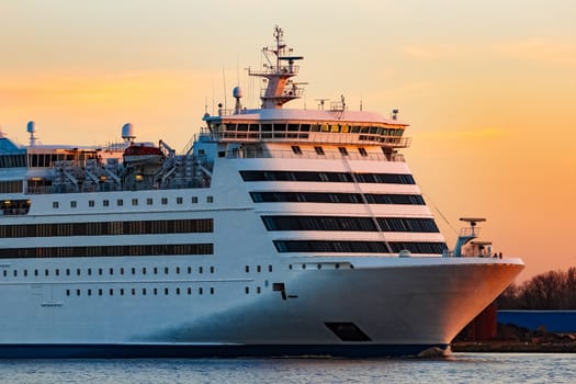 White passenger ship moving against the orange sunset sky