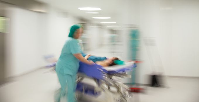 Motion blurred image of a nurse in hurry pushing litter down a sterile light hospital corridor.