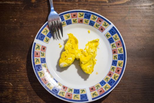 dish with butterfly-shaped omelette and fork on dark wooden table