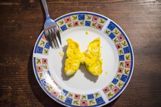 dish with butterfly-shaped omelette and fork on dark wooden table