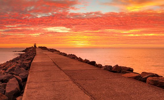 Standing on the breakwall with stunning sunrise skies of vivid reds and oranges.