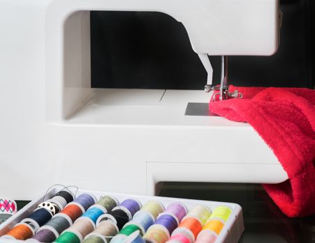 sewing machine and red cloth, sewing process in the phase of overstitching,colored spools.