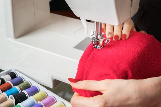 Young woman sewing fabric on sewing machine,sewing process in the phase of overstitchin,colored spools.