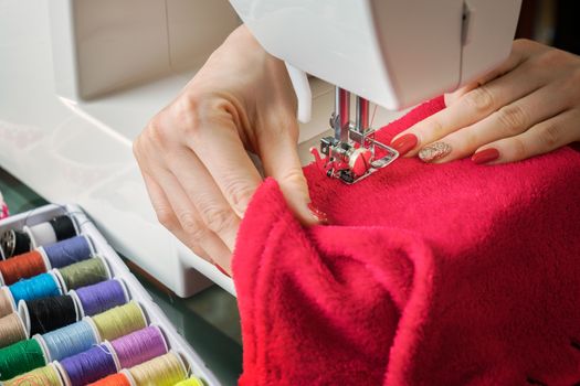 Young woman sewing fabric on sewing machine,sewing process in the phase of overstitchin,colored spools.