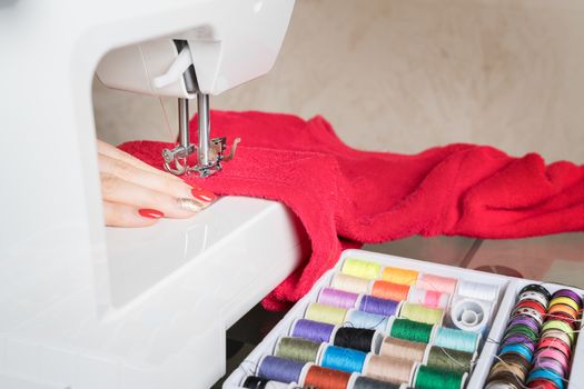 Young woman sewing fabric on sewing machine,sewing process in the phase of overstitchin,colored spools.