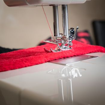 sewing machine close up and red cloth, sewing process in the phase of overstitching