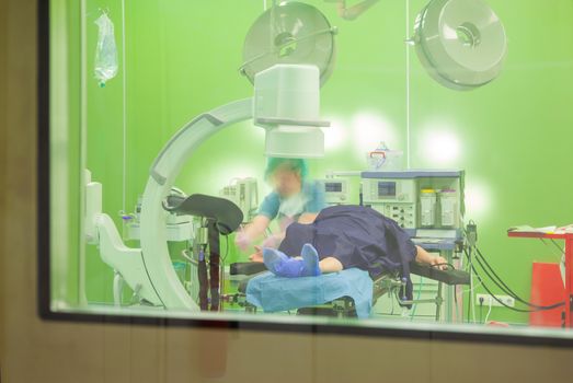 A blurred figure of a nurse is preparing a patient for operation in modern surgical room. View through a door.