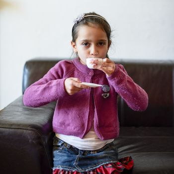 little girl plays, drinking tea on the sofa at home, lit by the window