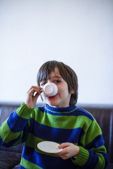 child plays, drinking tea on the sofa at home, lit by the window