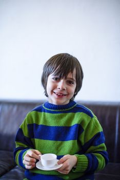 child plays, drinking tea on the sofa at home, lit by the window