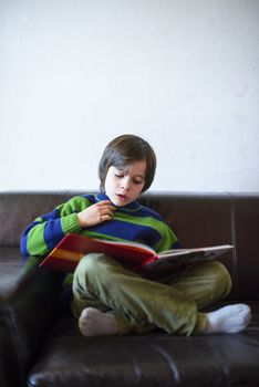 child reads a book sitting on the couch