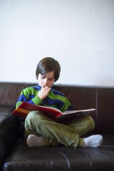 child reads a book sitting on the couch