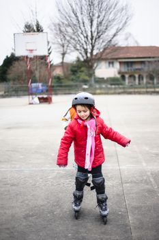 little girl learns to skate with rollerblading at the basketball court on a winter day