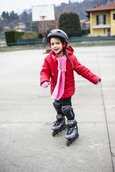 little girl learns to skate with rollerblading at the basketball court on a winter day