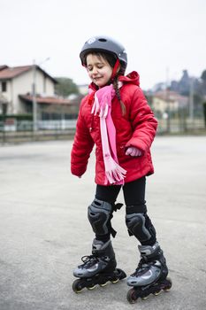 little girl learns to skate with rollerblading at the basketball court on a winter day