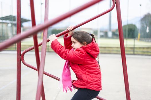 little girl climbs on iron frame of a basketball hoop in an outdoor basketball court