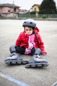 little girl learns to skate with rollerblading at the basketball court on a winter day and falls and looks disconsolate towards the camera