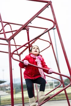 little girl climbs on iron frame of a basketball hoop in an outdoor basketball court