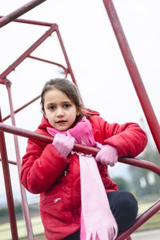 little girl climbs on iron frame of a basketball hoop in an outdoor basketball court