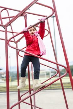 little girl climbs on iron frame of a basketball hoop in an outdoor basketball court