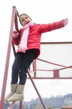 little girl climbs on iron frame of a basketball hoop in an outdoor basketball court