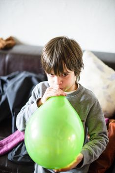 child inflates green balloon for birthday party in his home