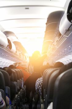 Friendly stewardess helping passenger to put luggage into cabin compartment.