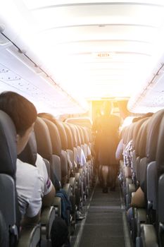 Interior of airplane with passengers on seats and stewardess walking the aisle.