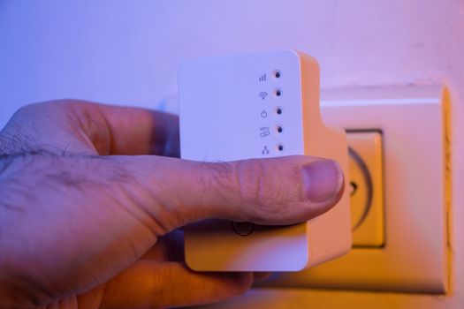 Man insert WiFi repeater into electrical socket on the wall. The device help to extend wireless network in home or office.