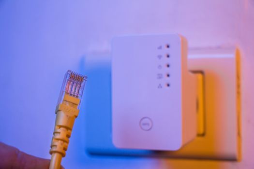 Closeup of ethernet cable. WiFi extender device in electrical socket on the wall on the background. The device is in access point mode that help to extend wireless network in home or office.