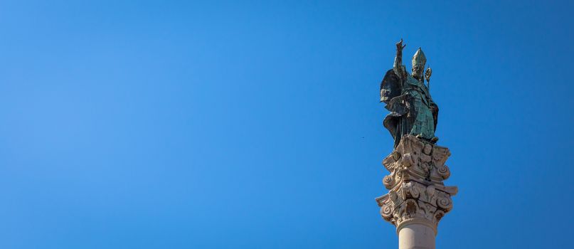 The symbol of Lecce town (Italy): Saint Oronzo (Sant'Oronzo) posed on the column at the center of the main town Square. Blue backgroud with copy space.