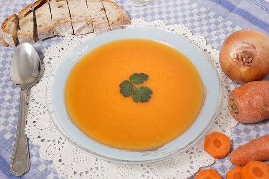 Homemade carrot soup on table cloth with onion and fruit.