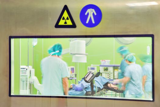 A view through the door window of a modern urology surgery with patient and motion blurred figures of doctors and nurses.