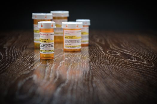 Variety of Non-Proprietary Prescription Medicine Bottles on Reflective Wooden Surface.