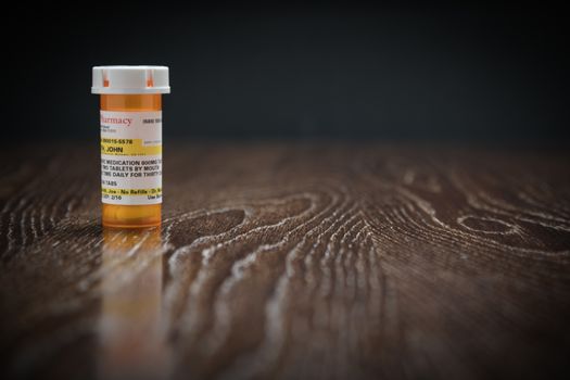 Non-Proprietary Prescription Medicine Bottle on Reflective Wooden Surface.