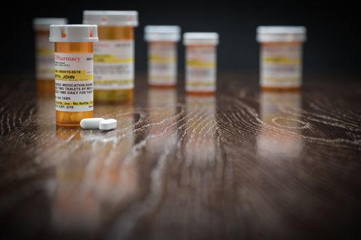 Variety of Non-Proprietary Prescription Medicine Bottles and Pills on Reflective Wooden Surface.