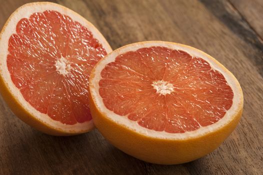 Close up view on fresh raw single pink grapefruit cut in half over dark wooden table