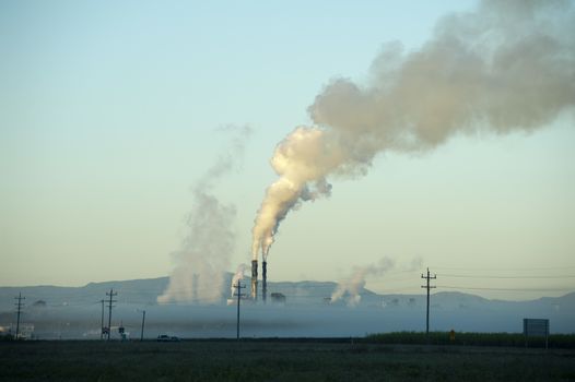 View of sugar processing plant behind fog or low clouds with stream piping up through smokestacks