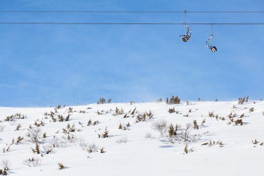 ski chair lift with two double seats, against blue sky, above snowy field