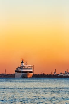 White passenger ship moving against the orange sunset sky