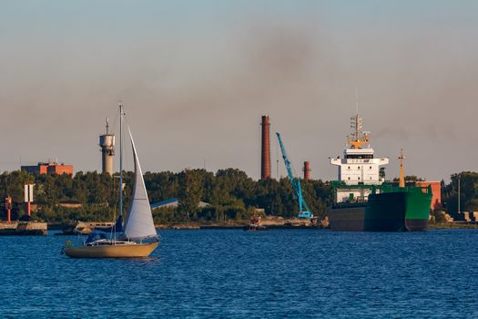 Green cargo ship leaves the port in a clear day