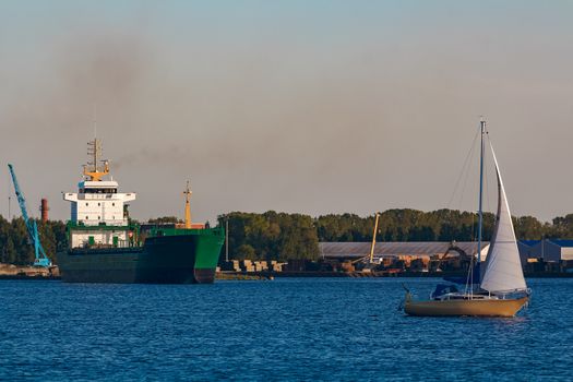 Green cargo ship leaves the port in a clear day