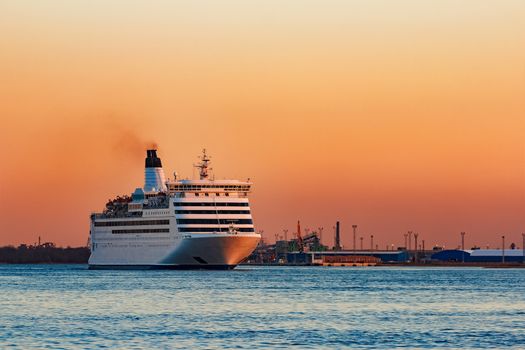 White passenger ship moving against the orange sunset sky