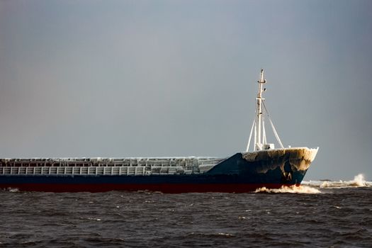 Blue bulk carrier moving from the sea in cold winter