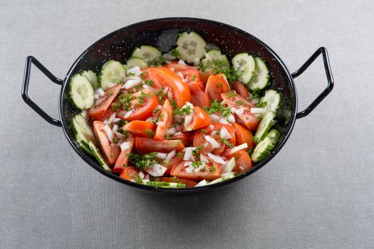 A bunch of sliced red tomatoes with cucumber and onion in a round metal bowl