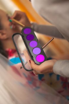 the make-up artist holds in his hand a set of eye shadows in the ultra violet range with a brush and does a make-up to the girl