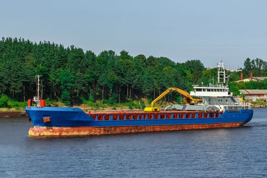 Blue cargo ship with long reach excavator moving to the port