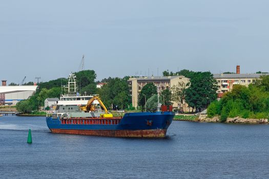 Blue cargo ship with long reach excavator moving to the port